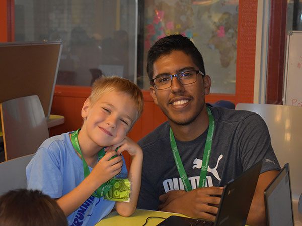 Summer camp volunteer in computer science education bonds with a young boy at camp